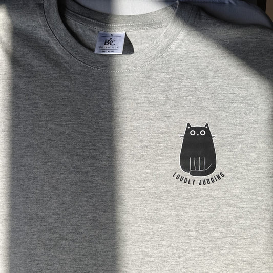 Detail van tekening van kat met opschrift ‘Loudly Judging’ op grijze t-shirt.