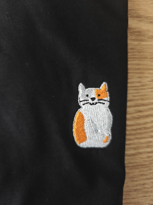 Detail van geborduurde ros/witte kat op zwarte katoenen t-shirt.
