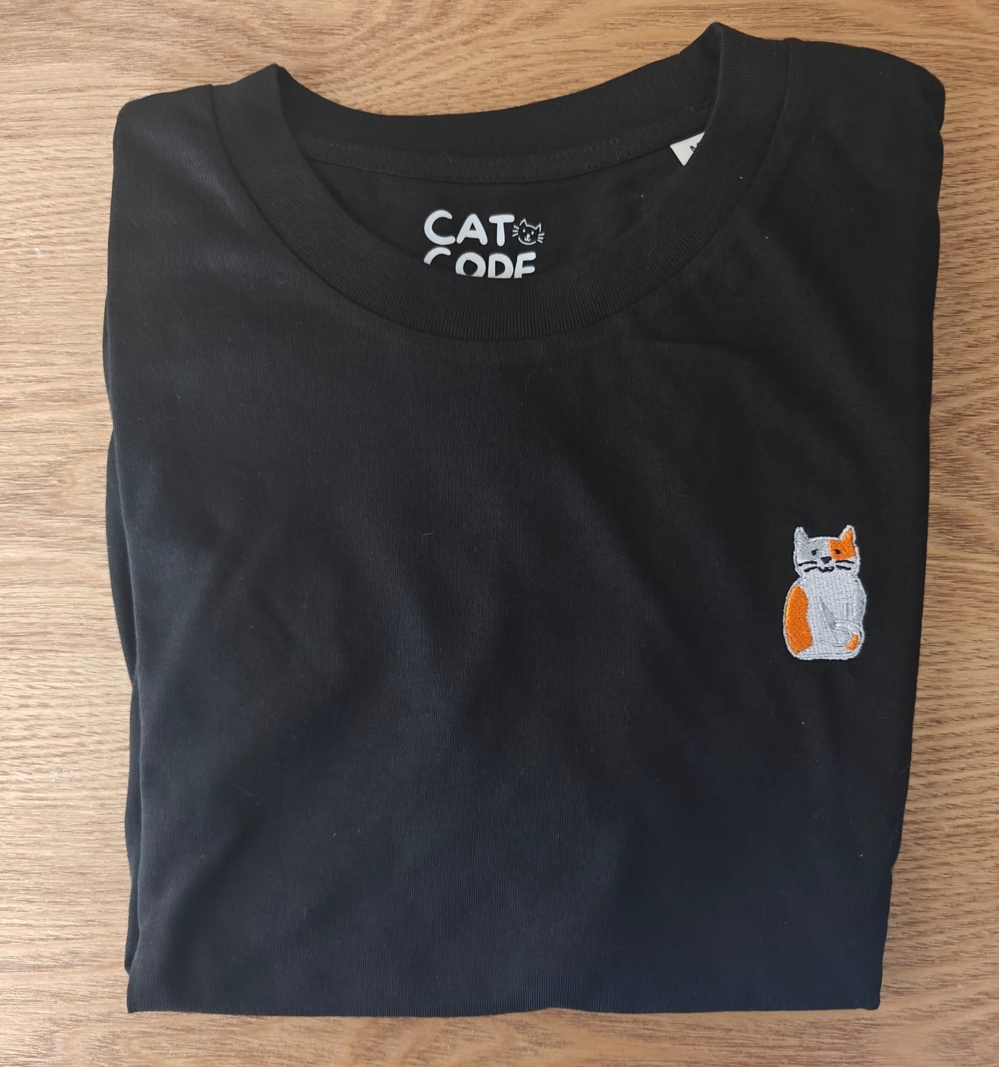 Detail van geborduurde ros/witte kat op zwarte katoenen t-shirt.
